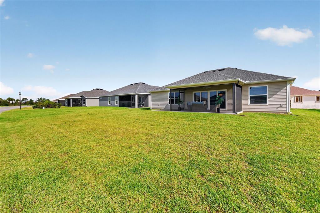 The rear exterior of a suburban house features a screened-in patio and a large lawn — 1742 JAMES GRAY STREET, THE VILLAGES, FL
