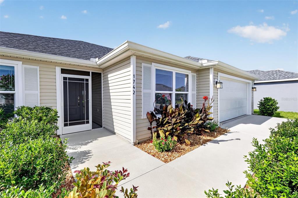 The exterior of a single-story house features light siding, a front door, and a garage — 1742 JAMES GRAY STREET, THE VILLAGES, FL