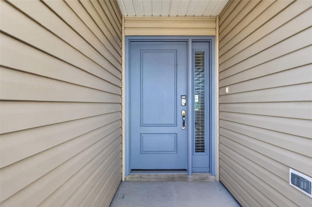 A blue front door with a side window is set between beige horizontal vinyl siding — 1742 JAMES GRAY STREET, THE VILLAGES, FL