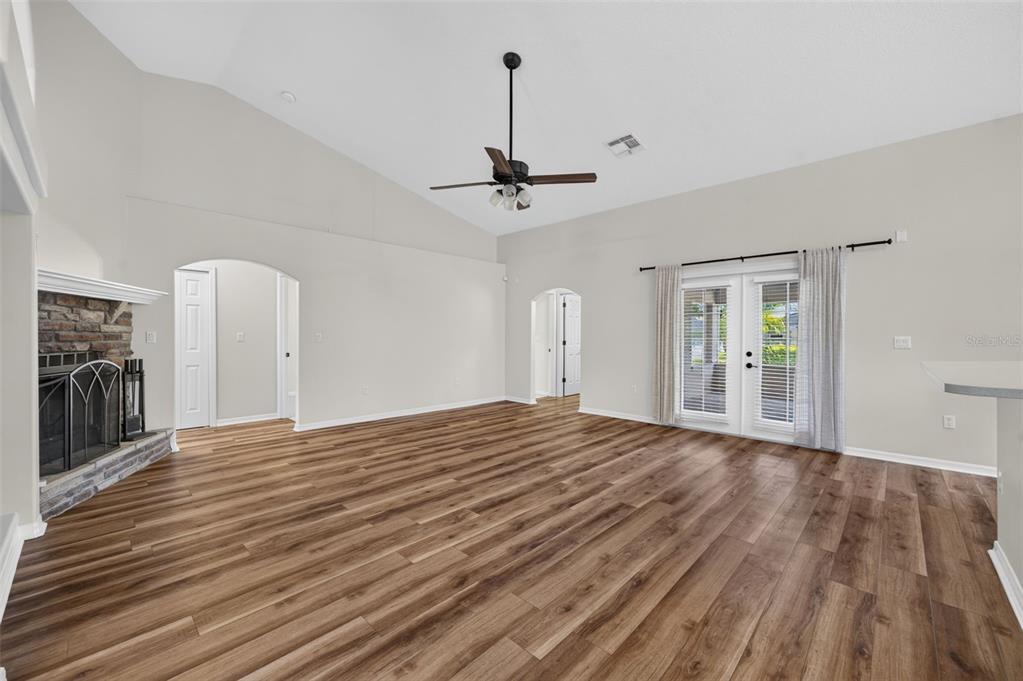 A spacious living room features vaulted ceilings, wood-look flooring, a stone fireplace, and French doors — 4911 RAYLENE WAY, ST CLOUD, FL