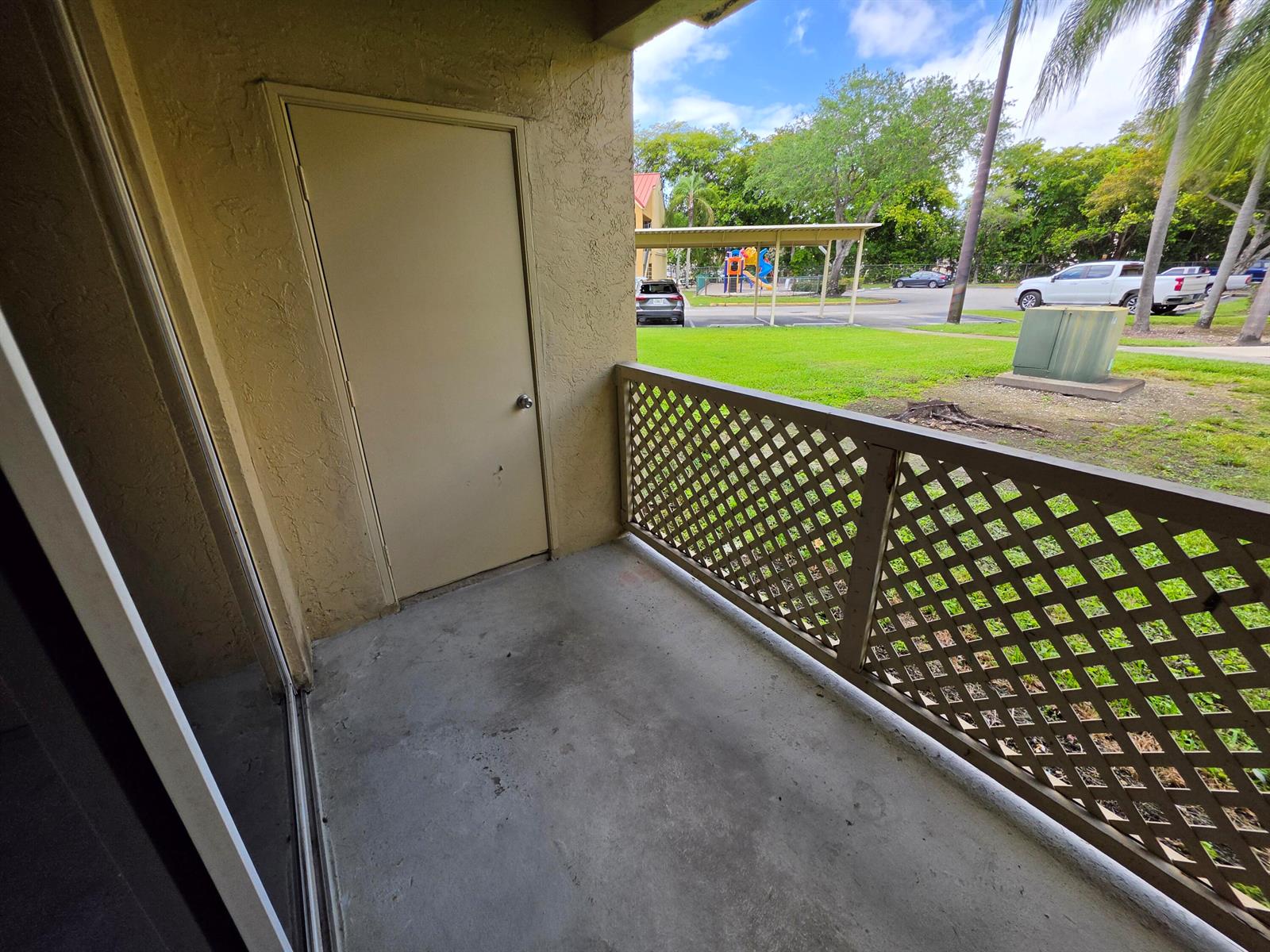 A covered balcony features a concrete floor, a storage closet door, and a lattice railing — 18340 NW 68th Avenue # F, Hialeah FL 33015, HIALEAH, FL