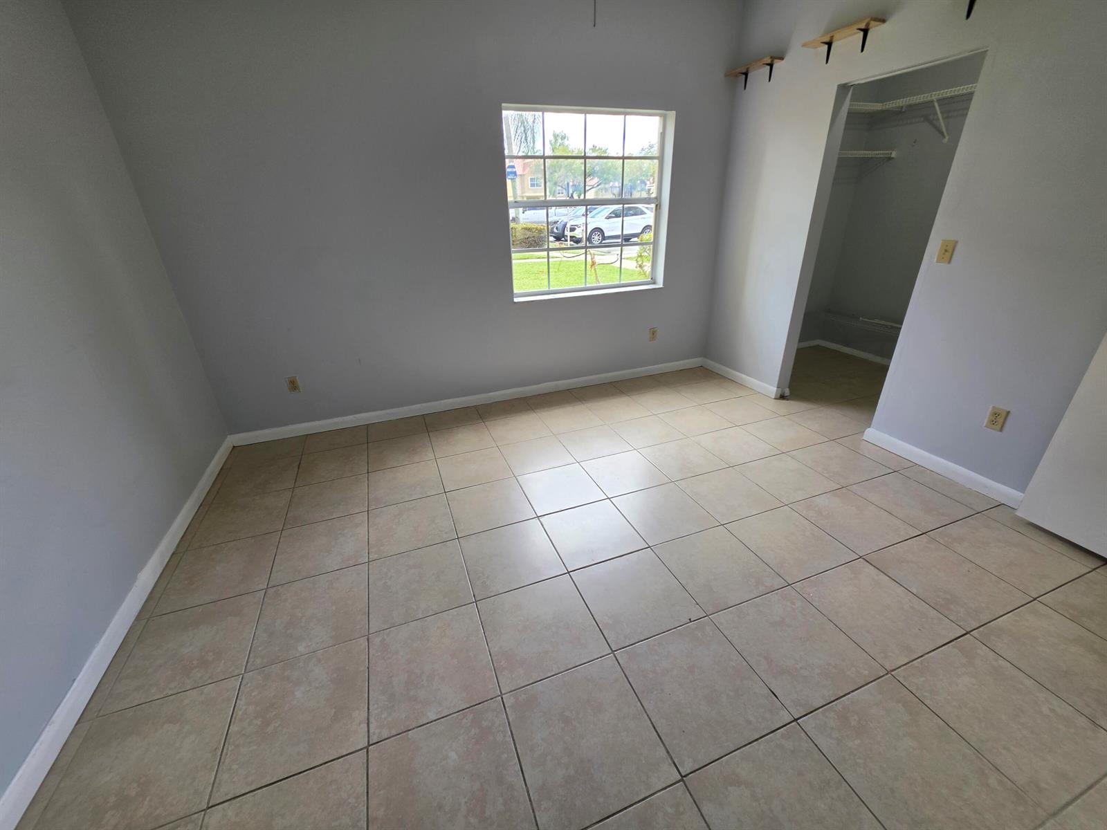 An empty bedroom features light gray walls, beige tile flooring, a window, and a closet — 18340 NW 68th Avenue # F, Hialeah FL 33015, HIALEAH, FL