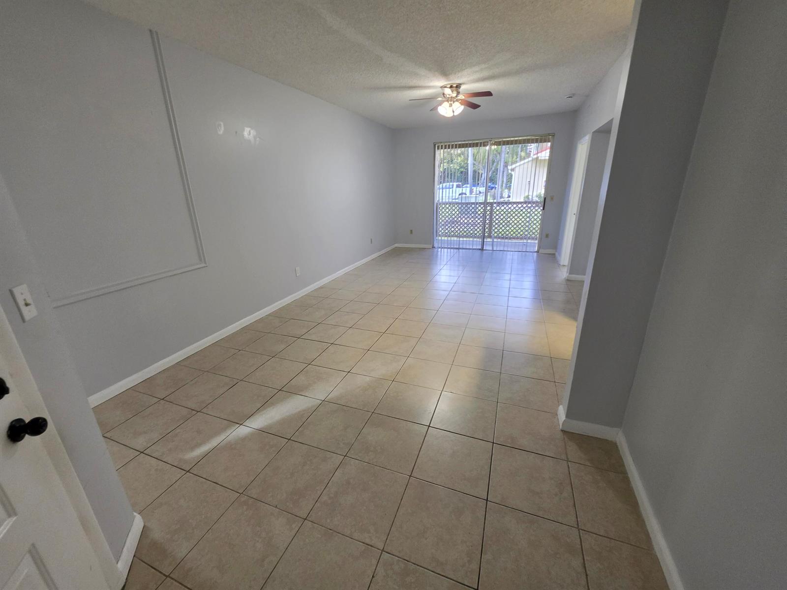 An empty room with light gray walls, beige tile flooring, and a sliding glass door — 18340 NW 68th Avenue # F, Hialeah FL 33015, HIALEAH, FL