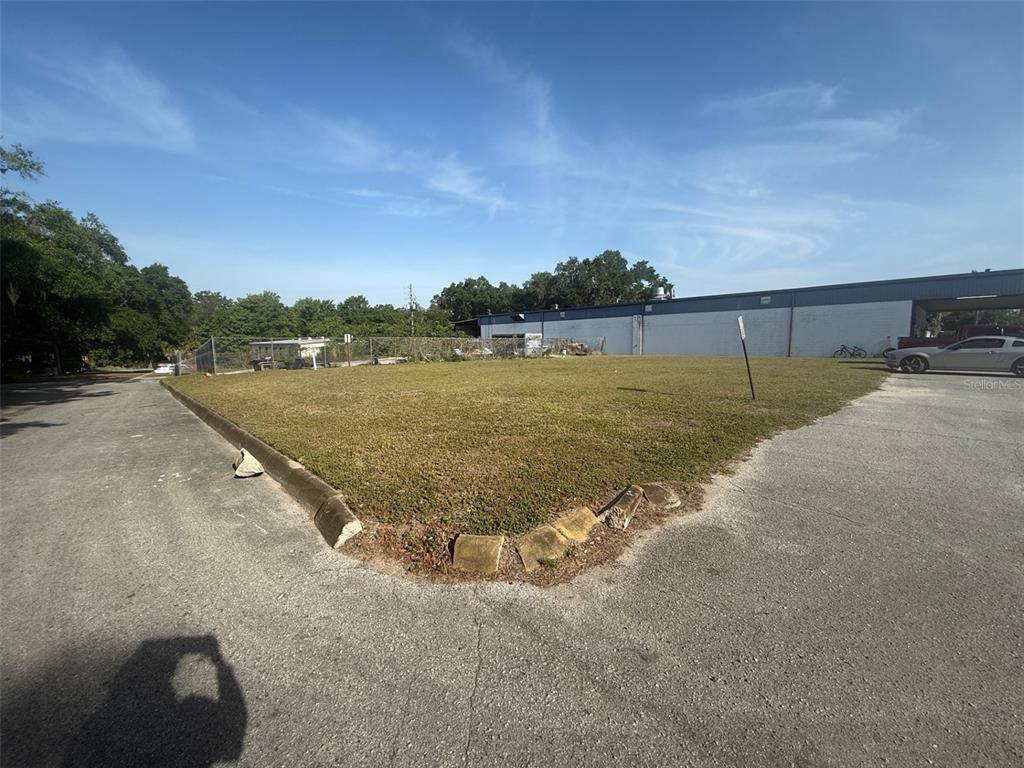 A grassy, vacant corner lot sits between an asphalt driveway and a large industrial building — SW 22 PLACE, OCALA, FL