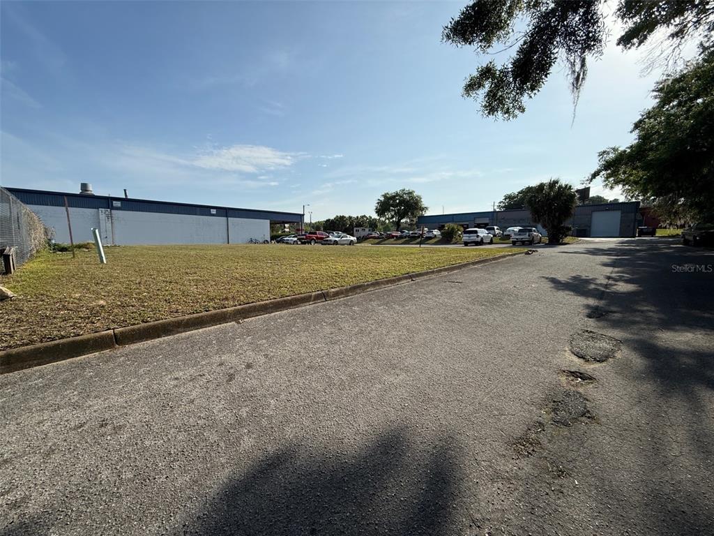 A paved road leads past a grassy lot toward commercial buildings under a blue sky — SW 22 PLACE, OCALA, FL