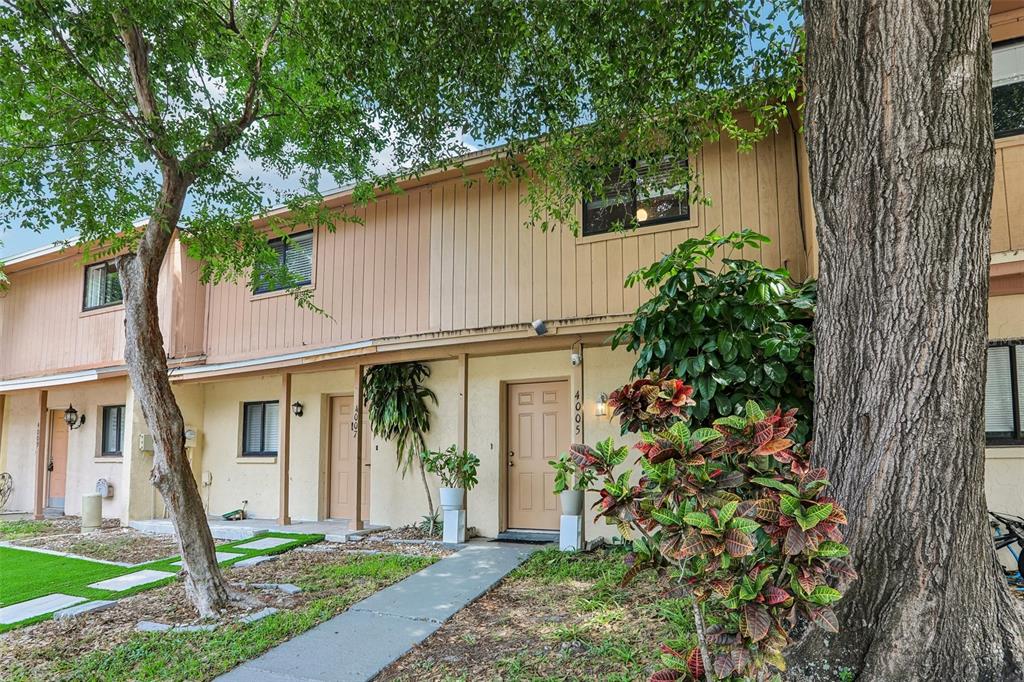 A two-story townhouse exterior features tan siding, a concrete walkway, and a large shade tree — 4005 OAK LIMB COURT, TAMPA, FL