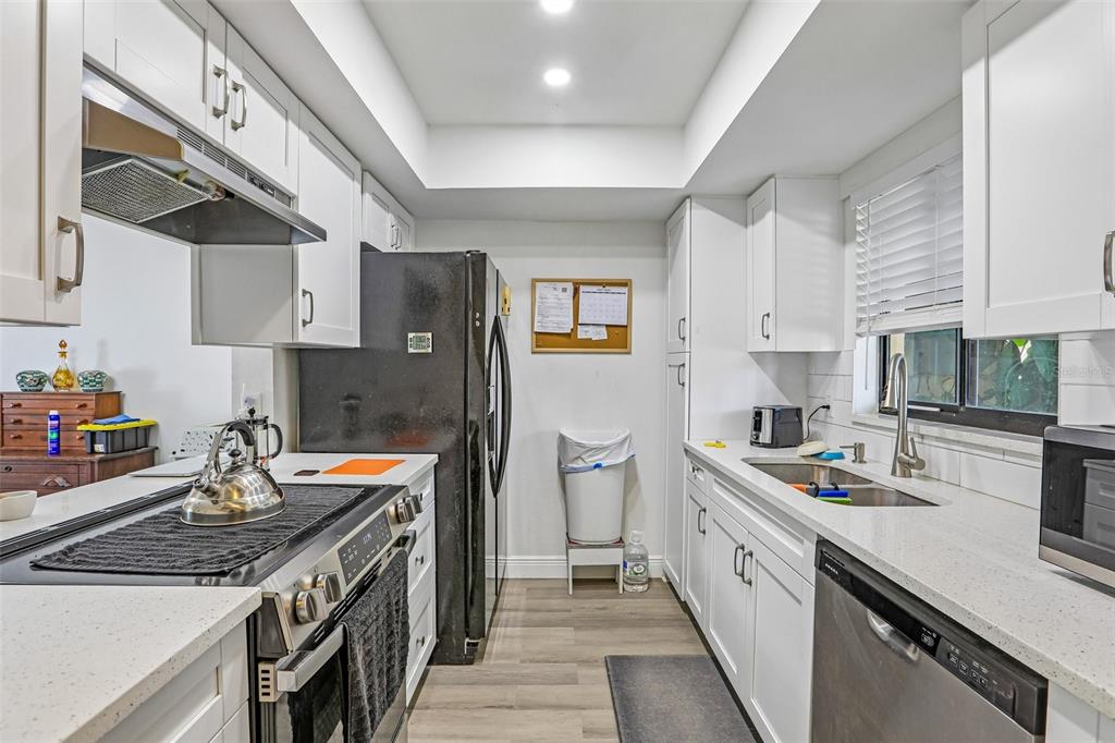 A galley-style kitchen features white cabinets, quartz countertops, stainless steel appliances, and wood-look flooring — 4005 OAK LIMB COURT, TAMPA, FL