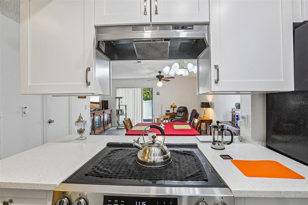 A kitchen stove with a kettle sits below a range hood overlooking a dining area — 4005 OAK LIMB COURT, TAMPA, FL