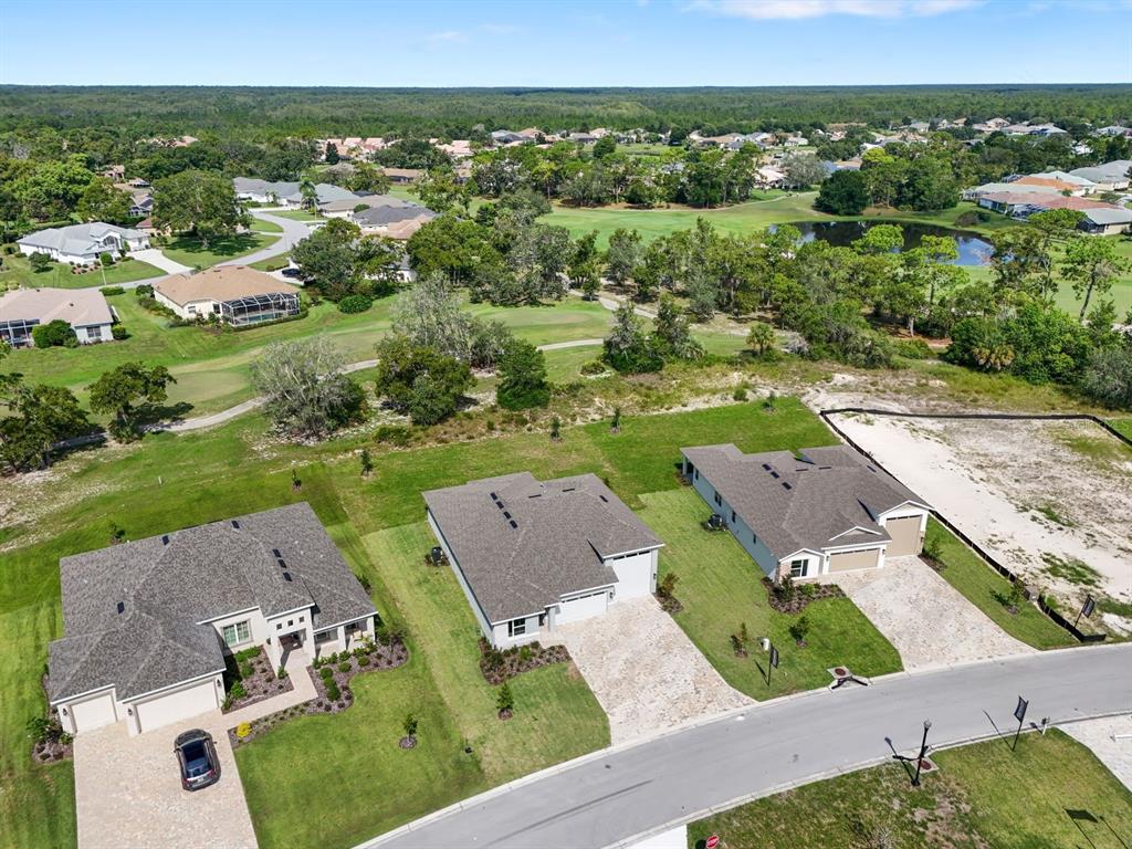 An aerial view shows three suburban houses with paved driveways bordering a golf course — 9005 PLAYERS DRIVE, WEEKI WACHEE, FL