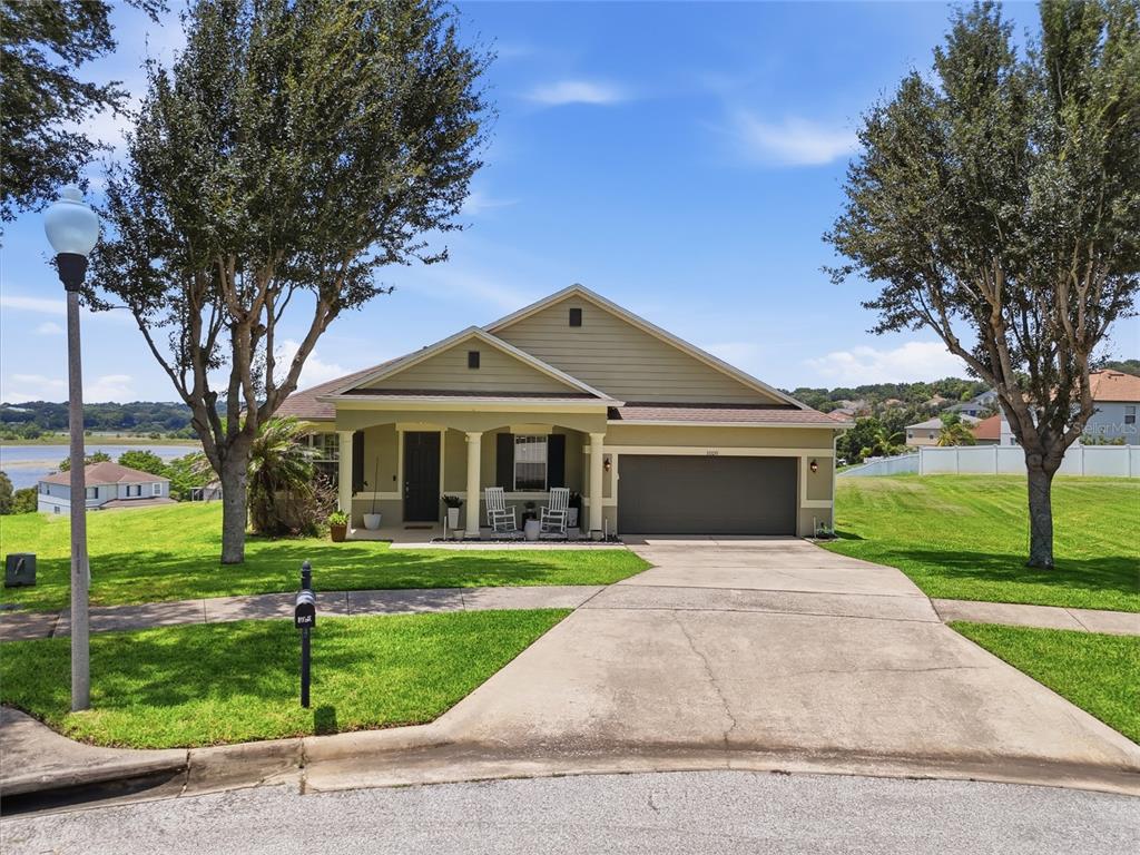 A single-story house with a two-car garage, front porch, and lawn sits near a lake — 1020 SAILING BAY DR, CLERMONT, FL