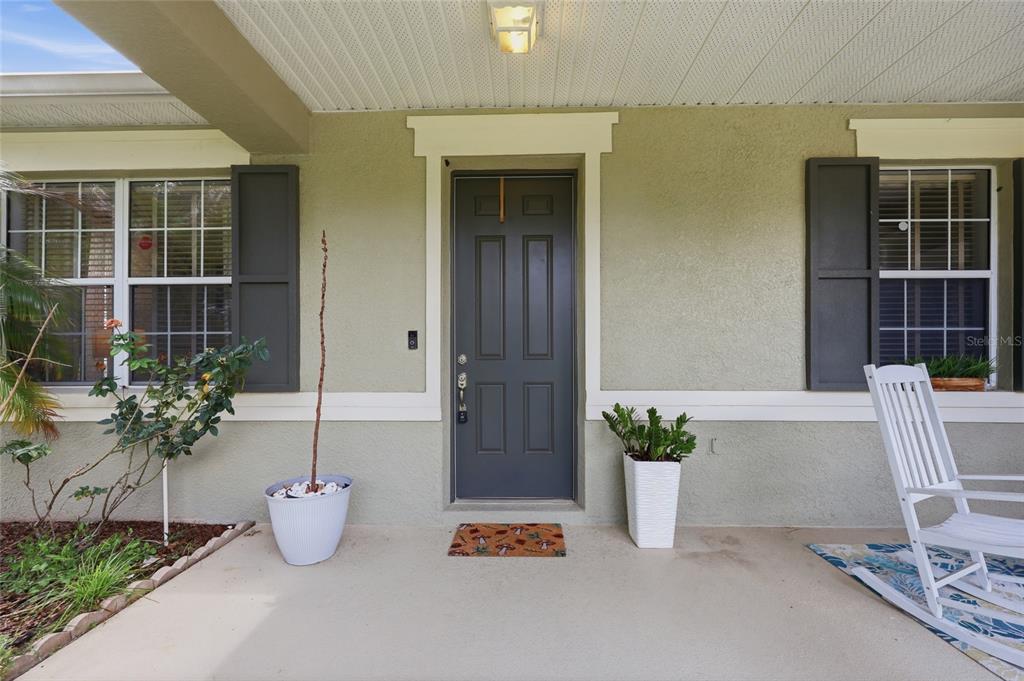 A covered front porch features a dark gray door, two windows with shutters, and a rocking chair — 1020 SAILING BAY DR, CLERMONT, FL