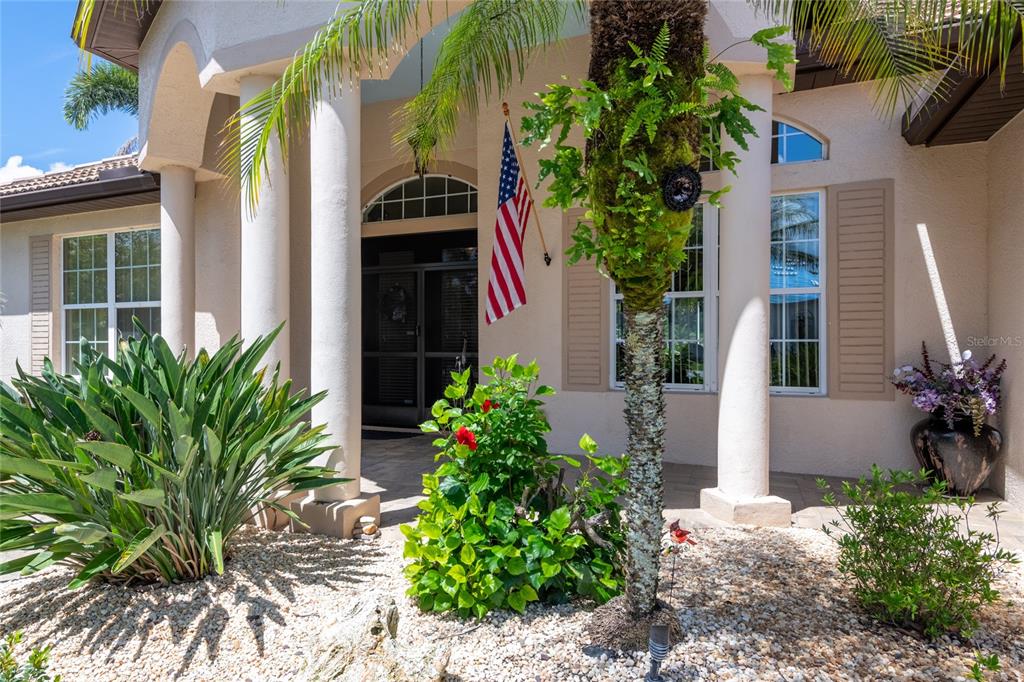 The exterior of a house features a covered entryway with columns, a palm tree, and an American flag — 21023 LOS CABOS COURT, LAND O LAKES, FL