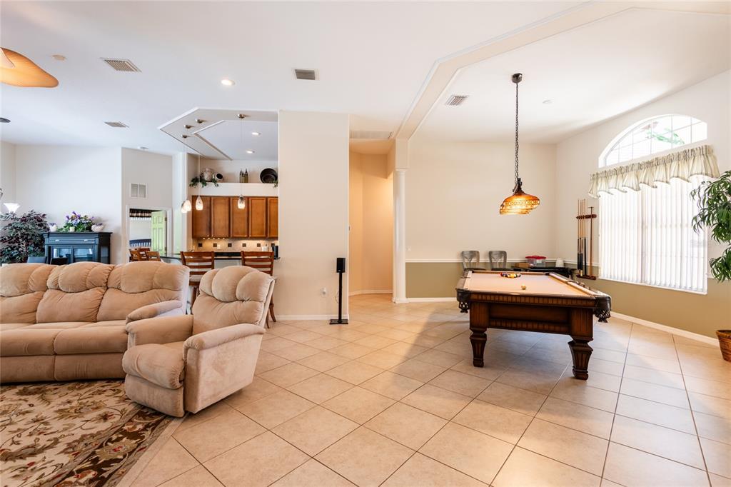 A living room with tile floors features a pool table and an open kitchen area — 21023 LOS CABOS COURT, LAND O LAKES, FL
