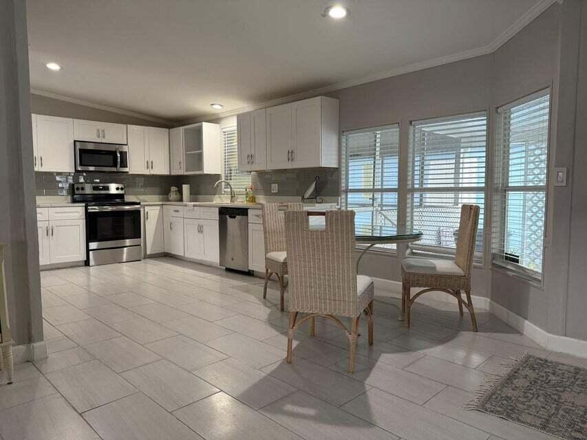 A kitchen with white cabinets, stainless steel appliances, and a dining area with wicker chairs — 6085 Seashore Drive, Atlantis FL 33462, ATLANTIS, FL