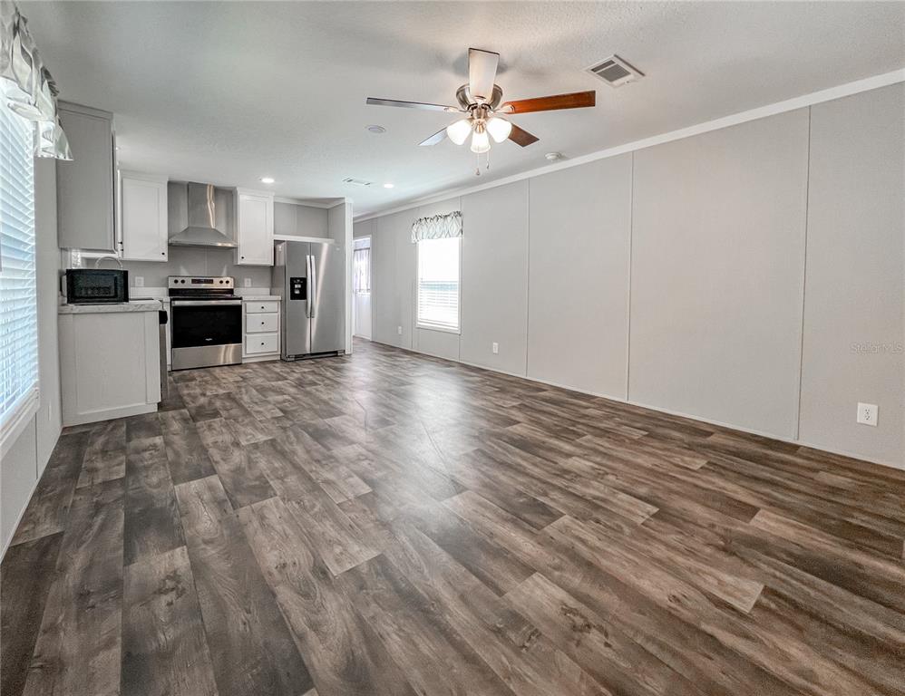 A kitchen and living area with wood-look flooring, white cabinets, and stainless steel appliances — 12203 LANTANA AVENUE, NEW PORT RICHEY, FL
