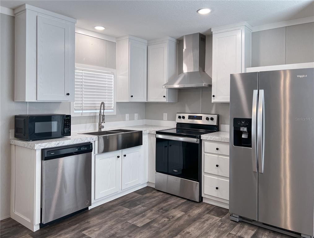 A kitchen features white cabinets, stainless steel appliances, a farmhouse sink, and wood-look flooring — 12203 LANTANA AVENUE, NEW PORT RICHEY, FL