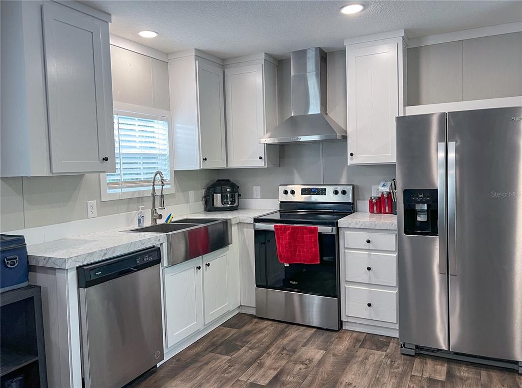 A kitchen features white cabinets, stainless steel appliances, a farmhouse sink, and wood-look flooring — 12203 LANTANA AVENUE, NEW PORT RICHEY, FL