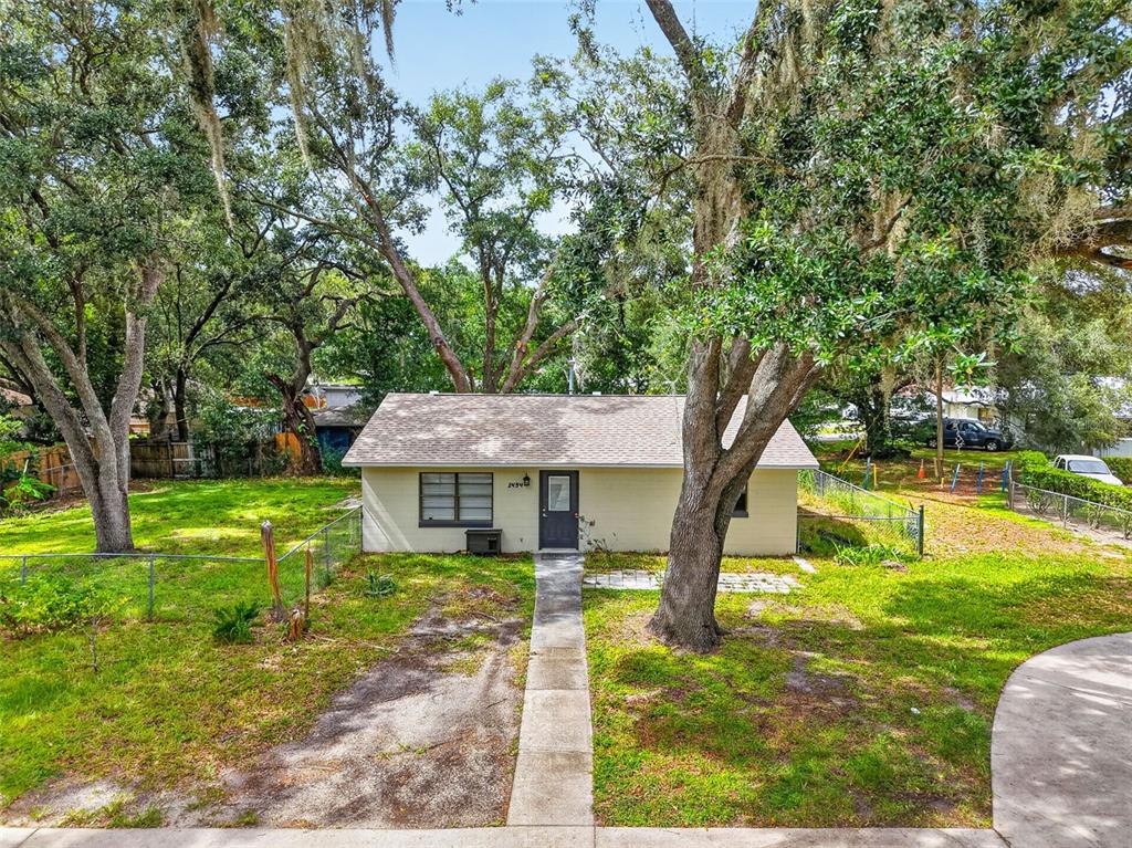 A small, light-colored house with a shingled roof sits on a grassy lot with trees — 1454 HOWARD STREET, GROVELAND, FL