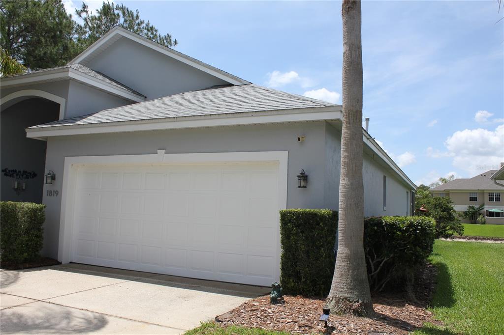 A gray house exterior features a white two-car garage door and a tall palm tree — 1819 SANDHILL LANE, WINTER HAVEN, FL