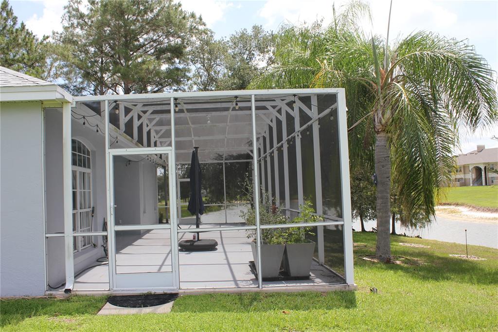 A screened-in patio with a gray floor, a door, and potted plants overlooking a pond — 1819 SANDHILL LANE, WINTER HAVEN, FL