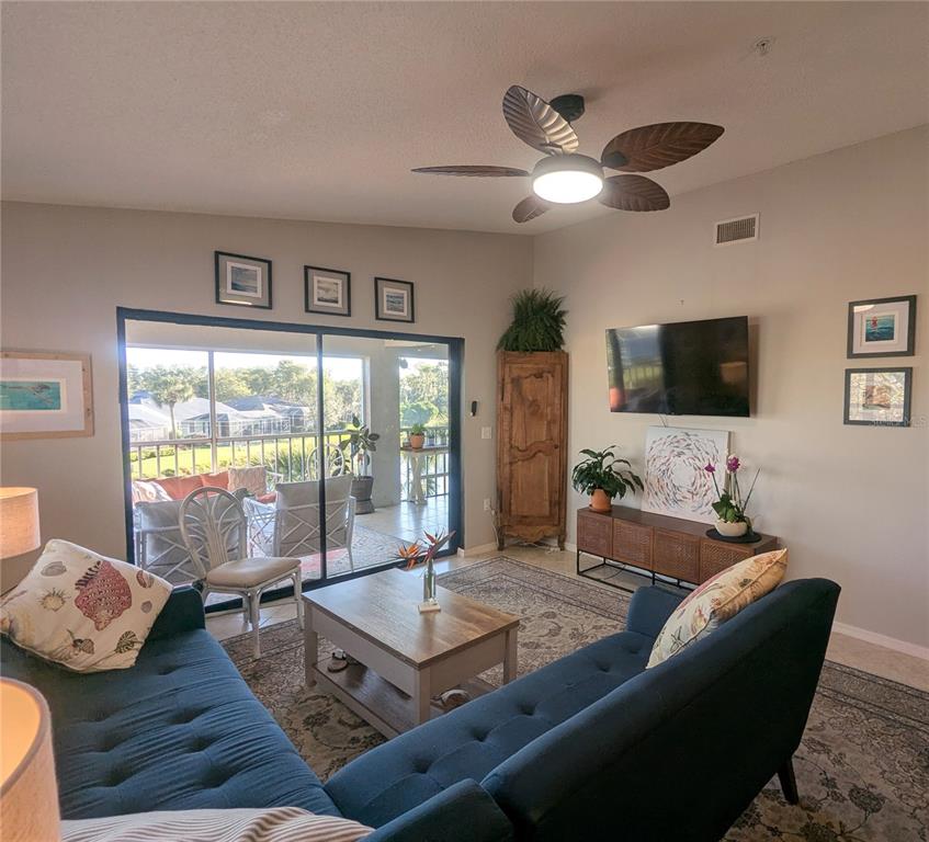 A living room features a blue sofa, a ceiling fan, and a sliding door to a patio — 9300 CLUBSIDE CIRCLE UNIT 1308, SARASOTA, FL