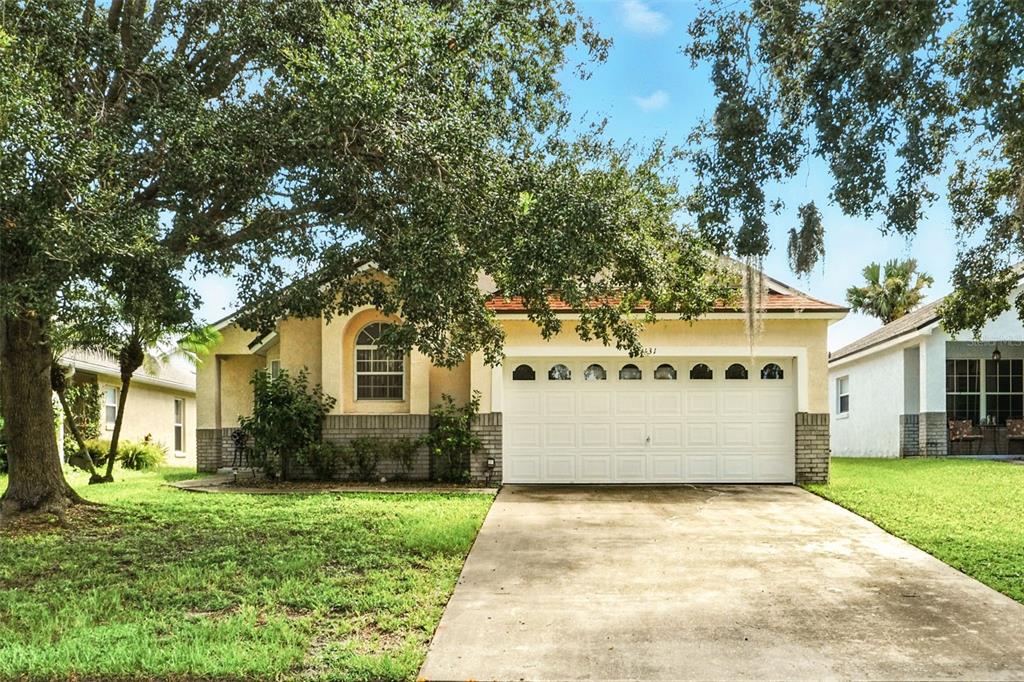 A single-story house with a white garage door, tan stucco siding, and a large oak tree — 131 S ROMA WAY, KISSIMMEE, FL