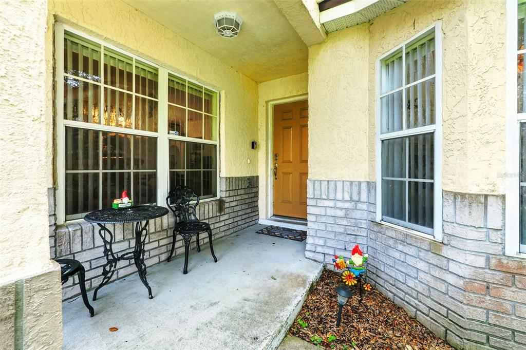 A covered front porch features a concrete floor, brick siding, and a tan front door — 131 S ROMA WAY, KISSIMMEE, FL