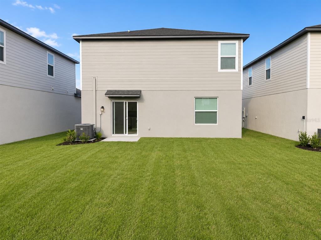 The rear exterior of a two-story house features light siding, a sliding door, and lawn — 2255 BLUE GROSBEAK PLACE, WIMAUMA, FL