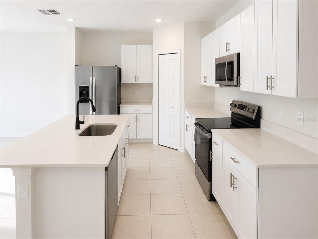 A modern kitchen features white cabinets, quartz countertops, stainless steel appliances, and a central island — 2255 BLUE GROSBEAK PLACE, WIMAUMA, FL