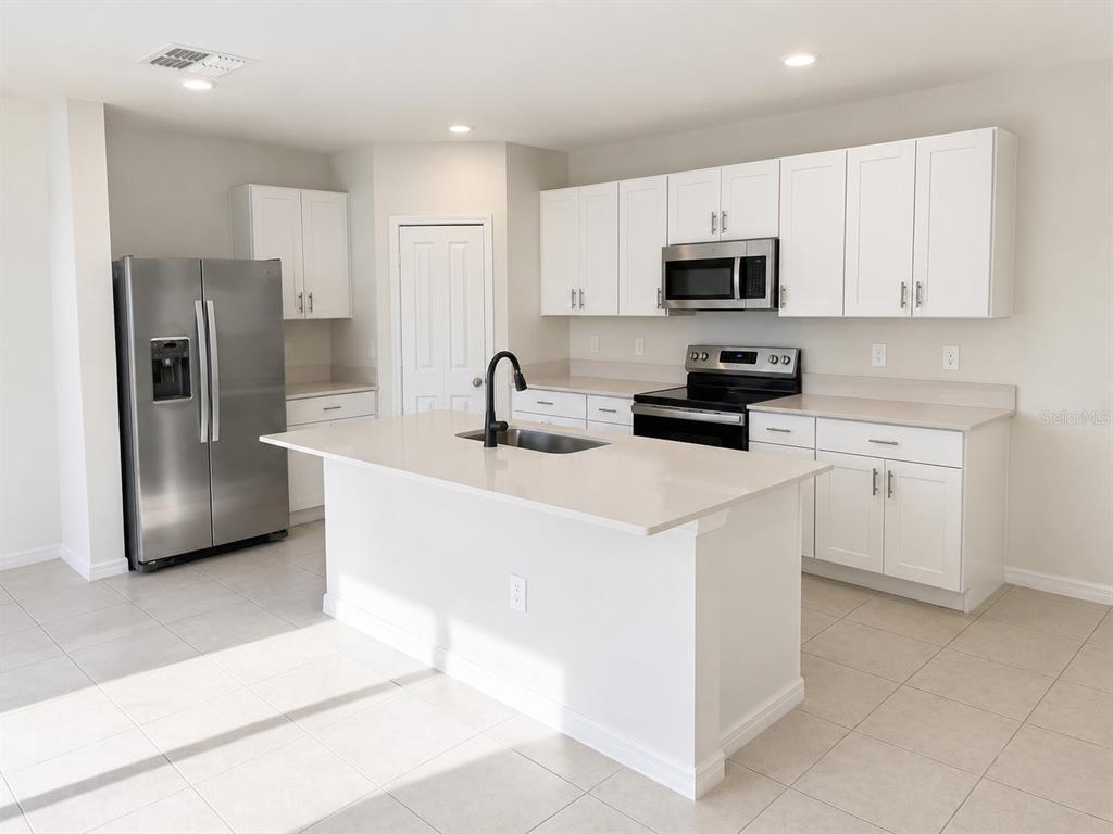 A modern kitchen features white cabinets, stainless steel appliances, and a central island with quartz countertops — 2255 BLUE GROSBEAK PLACE, WIMAUMA, FL