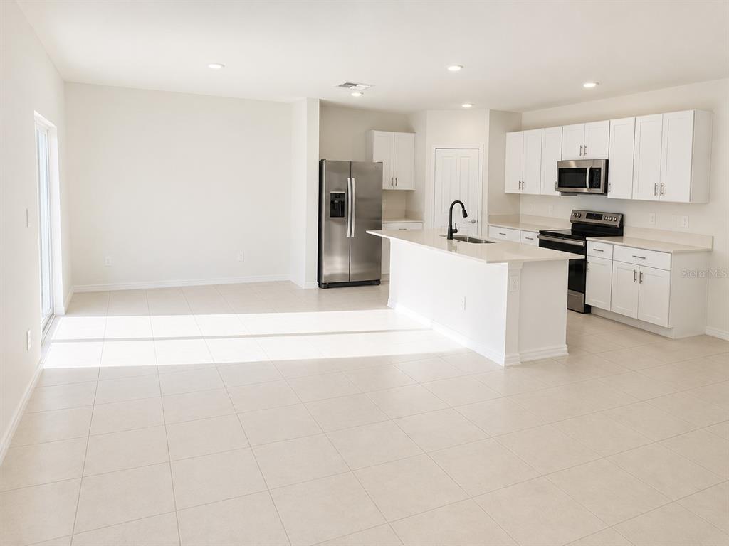 A bright, open-concept kitchen features white cabinetry, stainless steel appliances, and a central island — 2255 BLUE GROSBEAK PLACE, WIMAUMA, FL