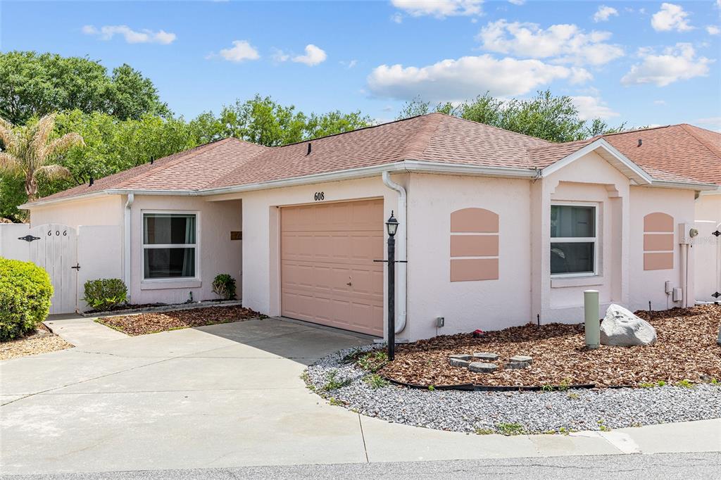 A single-story house with a pink exterior, a one-car garage, and a concrete driveway — 608 DELGADO AVENUE, THE VILLAGES, FL