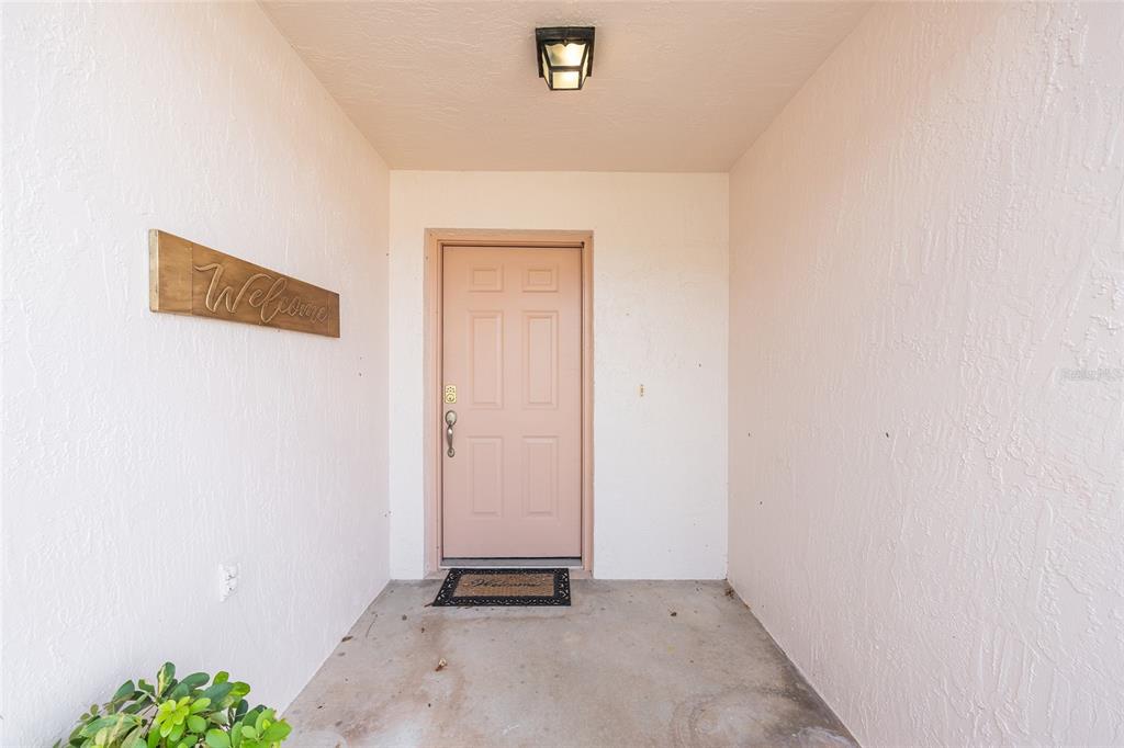 A light-colored front door with a welcome sign and mat sits in a covered entryway — 608 DELGADO AVENUE, THE VILLAGES, FL