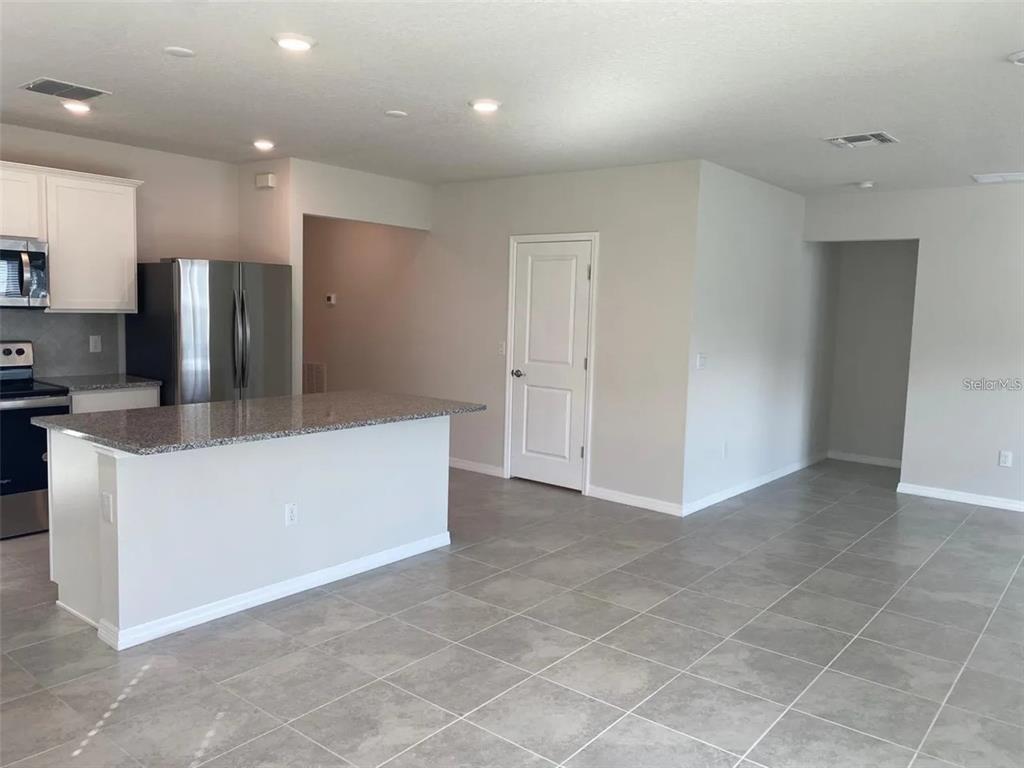 A kitchen with a granite island, stainless steel refrigerator, and light gray tile flooring — 9643 SUMMERS CAY CIRCLE, THONOTOSASSA, FL