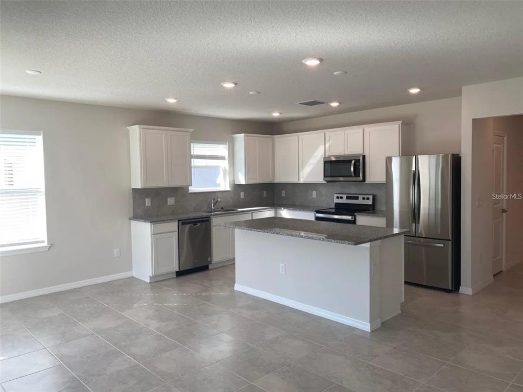 A kitchen with white cabinets, stainless steel appliances, a center island, and gray tile flooring — 9643 SUMMERS CAY CIRCLE, THONOTOSASSA, FL
