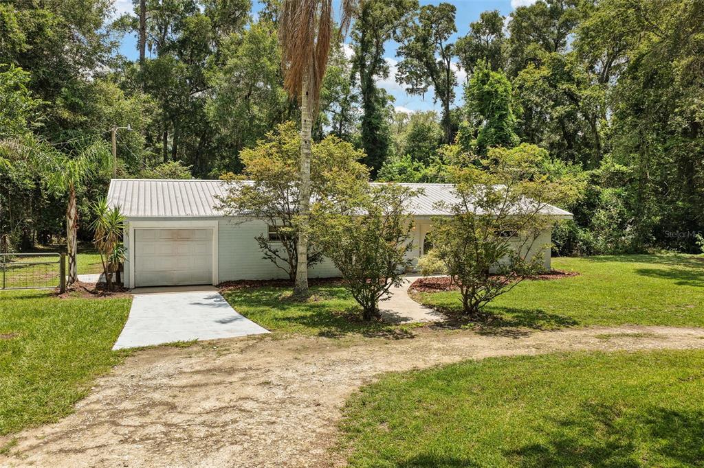 A single-story house with a metal roof, attached garage, and a dirt driveway — 3151 NE 176TH TERRACE, WILLISTON, FL