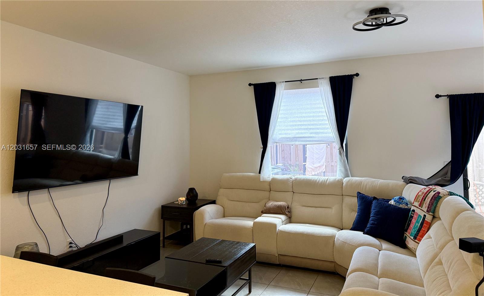 A living room features a white sectional sofa, a wall-mounted television, and dark furniture — 23049 SW 129th Pl, Miami FL 33170, MIAMI, FL