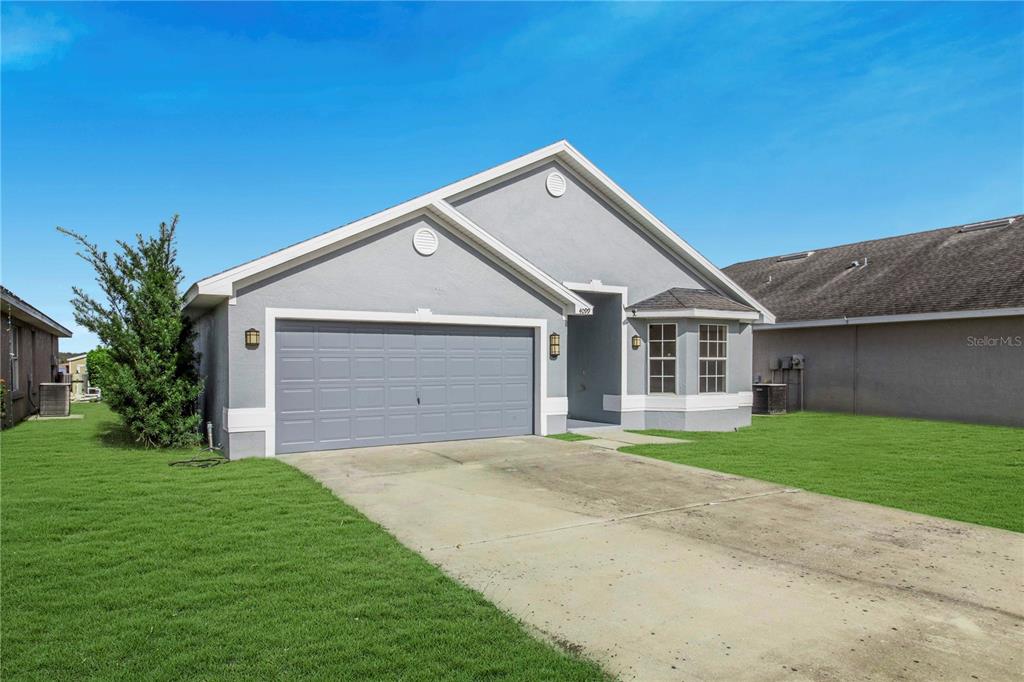 A gray single-story house features a two-car garage, a bay window, and a concrete driveway — 4099 ISLAND LAKES DRIVE, WINTER HAVEN, FL