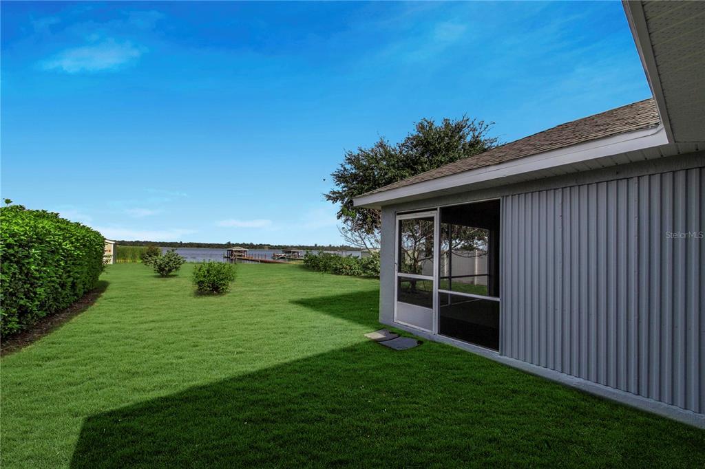 A grassy backyard with a screened-in porch overlooks a lake with a wooden dock — 4099 ISLAND LAKES DRIVE, WINTER HAVEN, FL