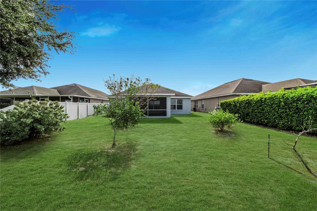 A grassy backyard features a screened-in patio, a white vinyl fence, and mature hedges — 4099 ISLAND LAKES DRIVE, WINTER HAVEN, FL