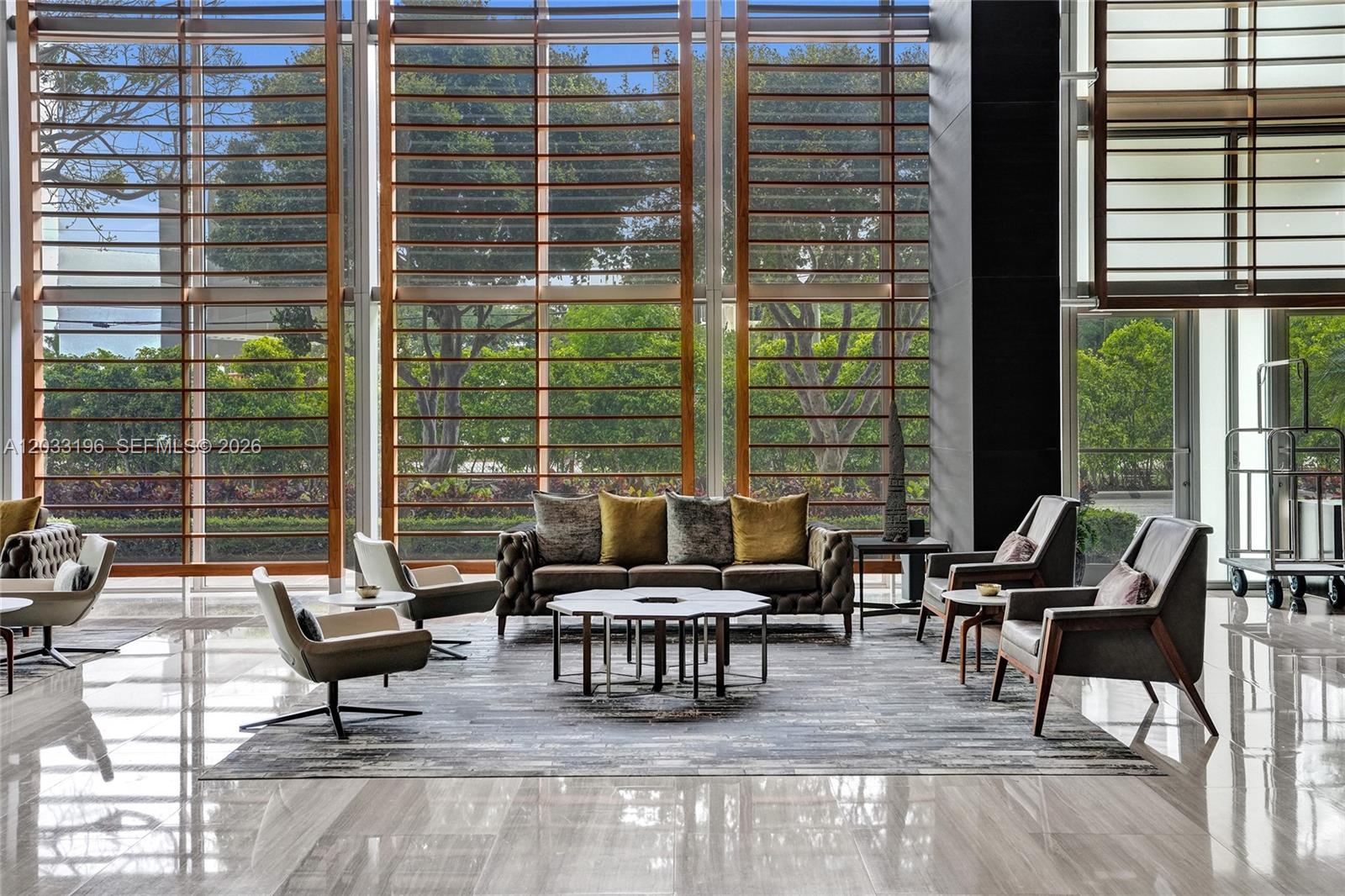 A modern lobby features floor-to-ceiling windows, a tufted sofa, and several armchairs on a rug — 3470 E Coast Ave # H1205, Miami FL 33137, MIAMI, FL