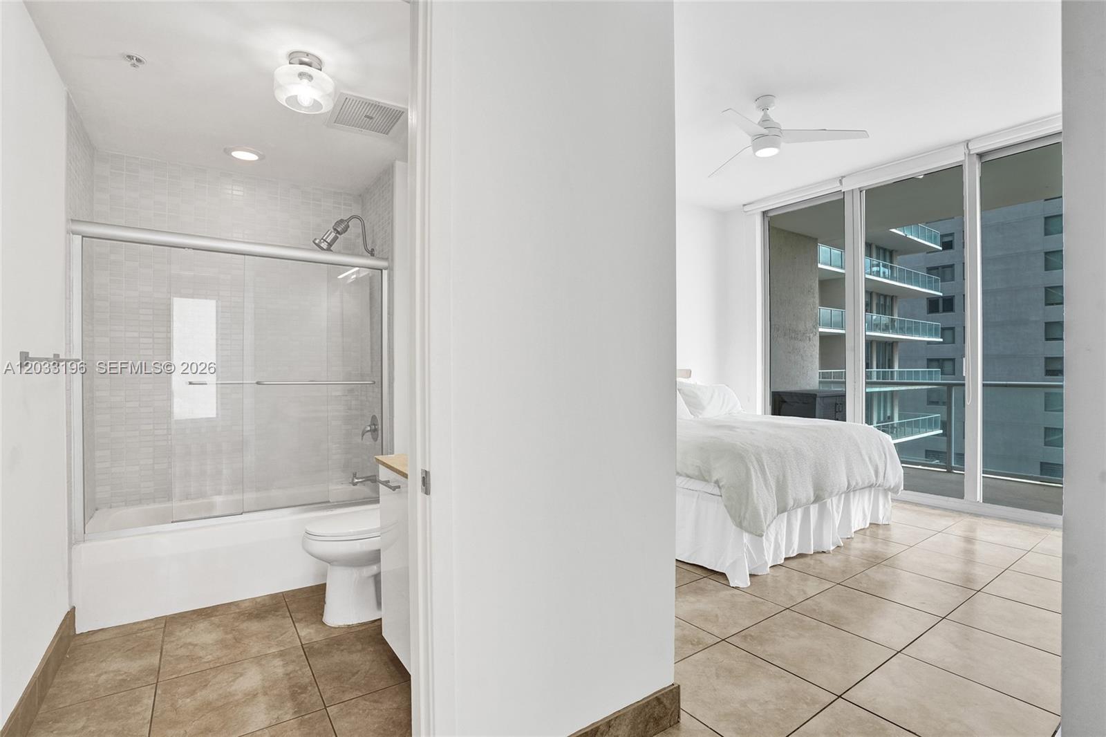A bathroom with a tub-shower combo sits adjacent to a bedroom with floor-to-ceiling windows — 3470 E Coast Ave # H1205, Miami FL 33137, MIAMI, FL