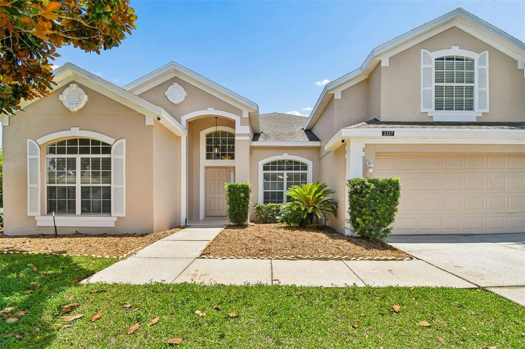 A single-story beige house with a two-car garage, arched windows, and a concrete walkway — 2337 TREYMORE DRIVE, ORLANDO, FL