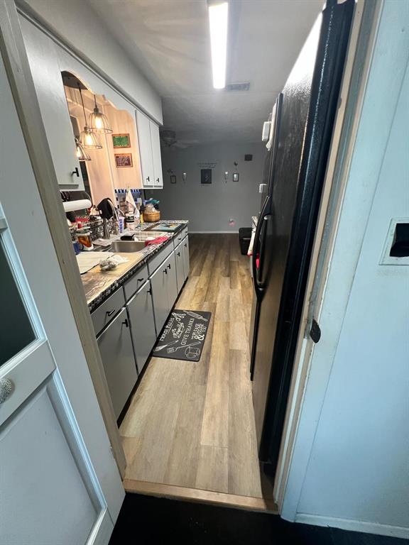 A galley kitchen features gray cabinets, wood-look flooring, and a black refrigerator — 1105 TIVOLI DRIVE, DELTONA, FL