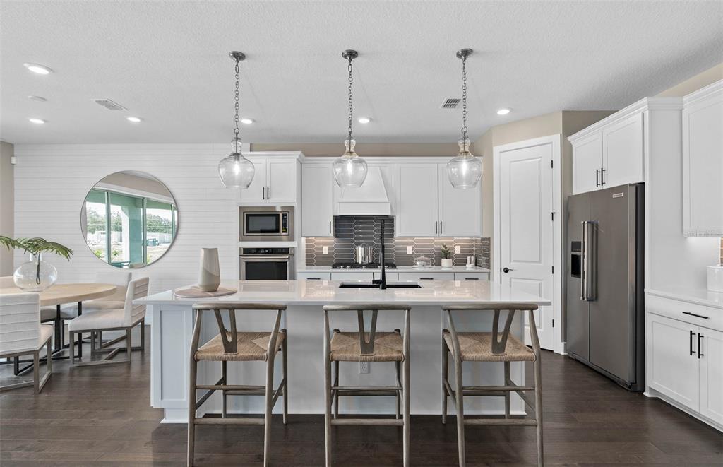 A modern kitchen features white cabinetry, a large island with bar seating, and pendant lights — 4990 GOOD DAY LANE, WEST MELBOURNE, FL