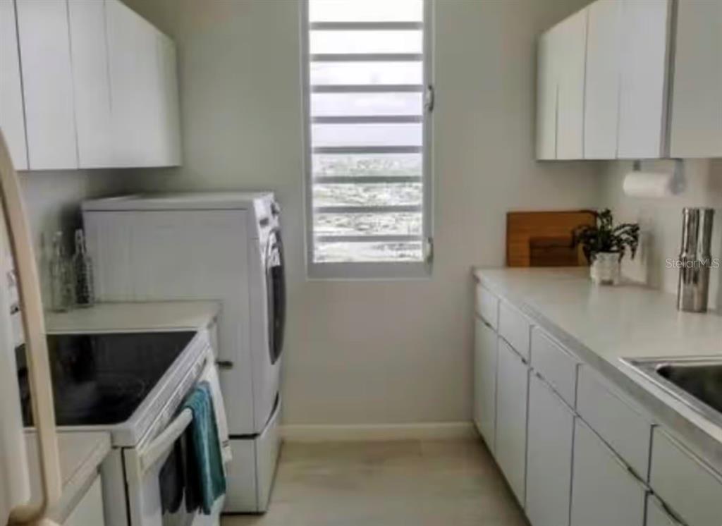 A galley-style kitchen features white cabinets, white countertops, a stove, and a laundry appliance — 1610 PLAYA AZUL, TOWER 3 UNIT 1610, LUQUILLO, PR