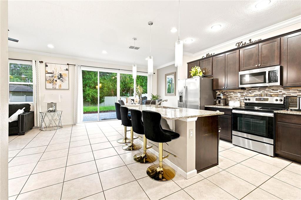 A kitchen with dark cabinets, granite countertops, and a breakfast bar with three stools — 3821 PINEWOOD GARDENS BOULEVARD, ST CLOUD, FL