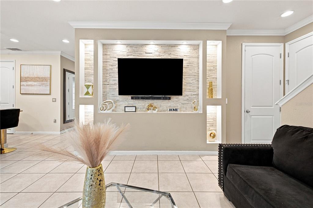 A living room features a stone-accented media wall with built-in shelving and tile flooring — 3821 PINEWOOD GARDENS BOULEVARD, ST CLOUD, FL
