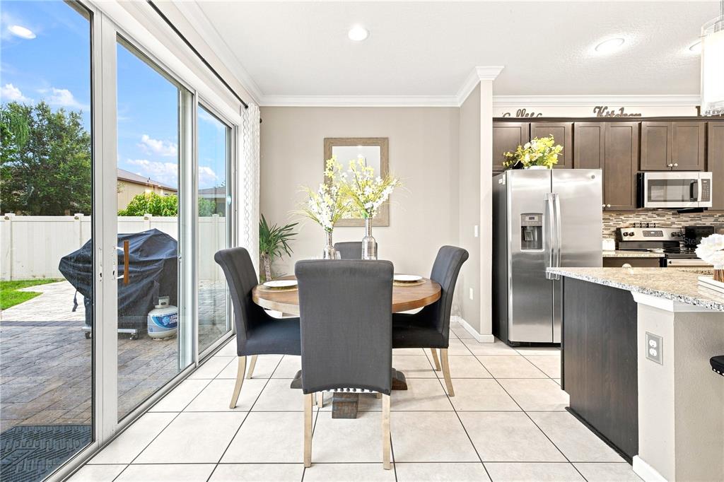 A dining area with a round table, dark chairs, tile flooring, and an adjacent kitchen — 3821 PINEWOOD GARDENS BOULEVARD, ST CLOUD, FL