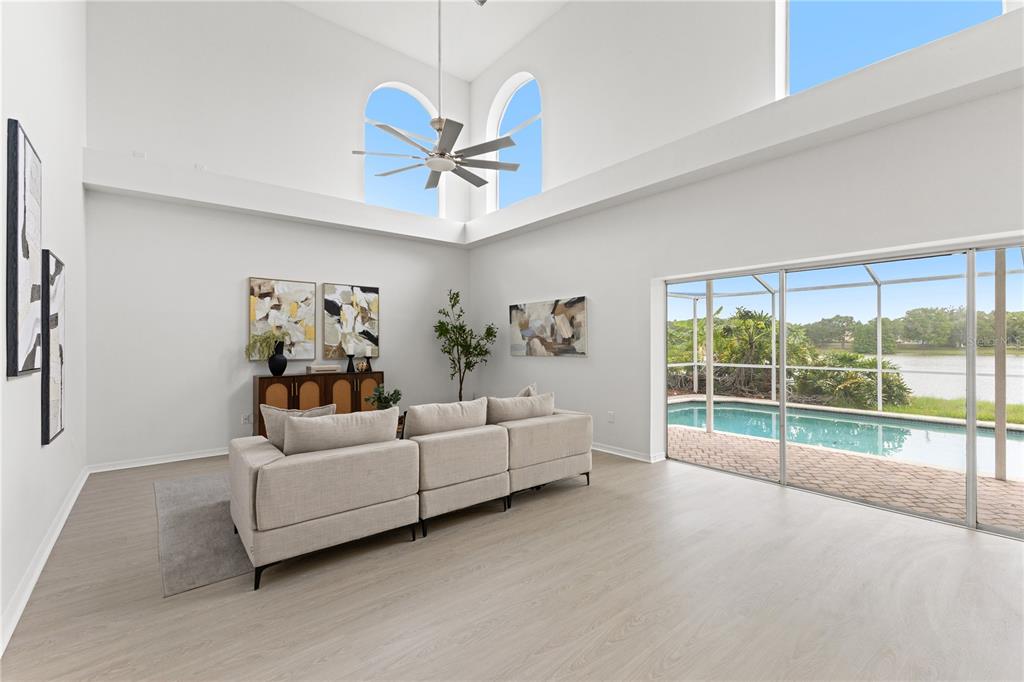 A bright living room features high ceilings, a ceiling fan, and sliding doors to a pool — 11503 WHISPERING HOLLOW DRIVE, TAMPA, FL